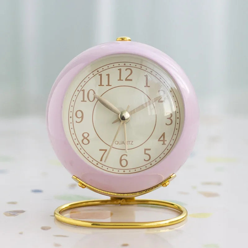 Pink round alarm clock with a cream numbered face, gold-coloured hands and circular stand