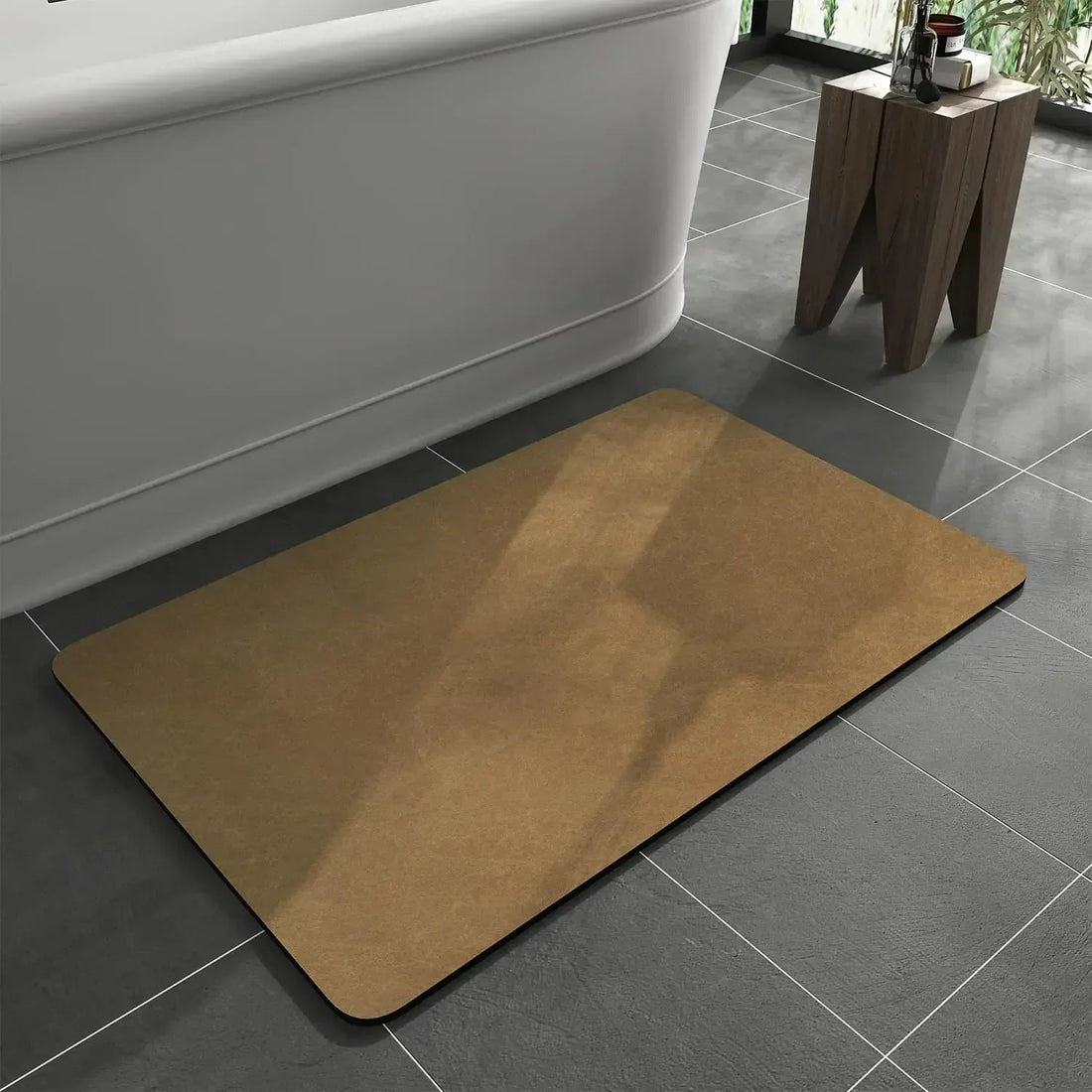 Ochre rectangular bath mat with rounded corners on grey tiles beside a white bath and small wooden stool