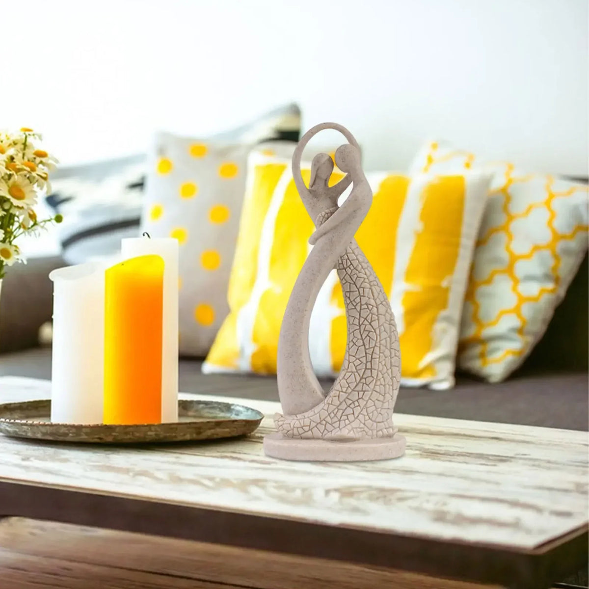Beige abstract dancing couple sculpture on a coffee table beside yellow candles and a sofa with yellow cushions