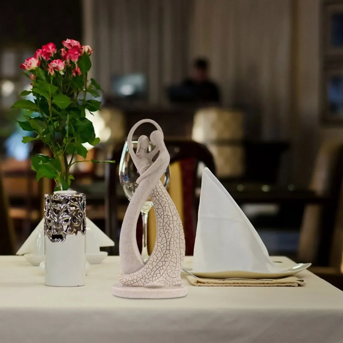 Beige abstract dancing couple sculpture displayed on a dining table beside flowers and folded napkins
