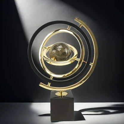 Black and gold-coloured ring sculpture with a central marbled sphere casting a shadow in sunlight.