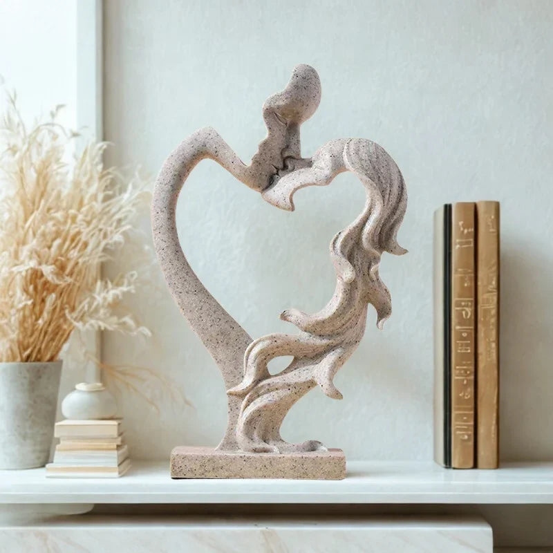 Beige textured kissing couple sculpture with an open heart-shaped centre on a shelf beside books and dried stems