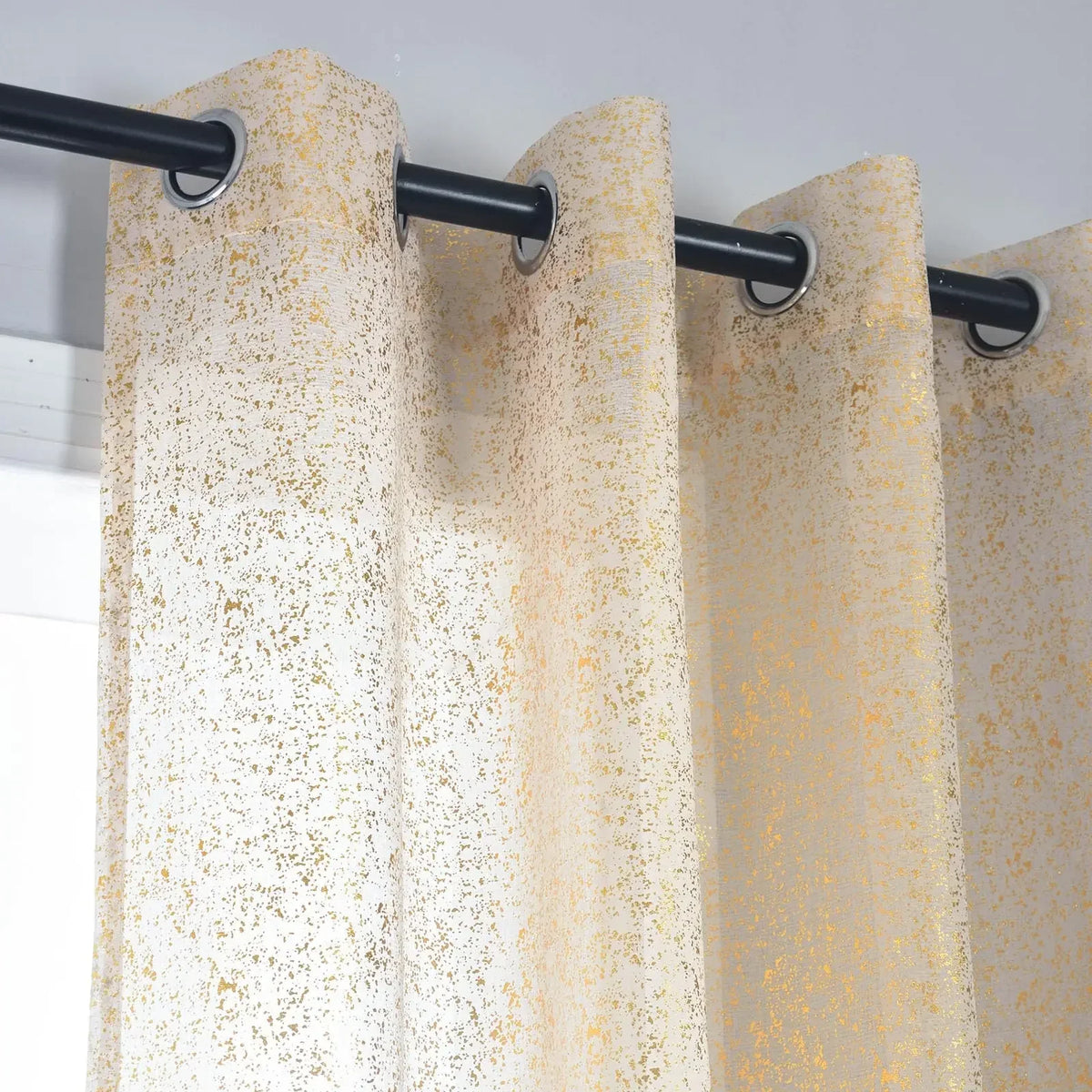Close-up of beige sheer curtain panels threaded through eyelets on a black curtain rod.