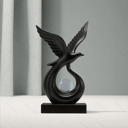Front view of a black bird sculpture with raised wings and a clear sphere on a black base.