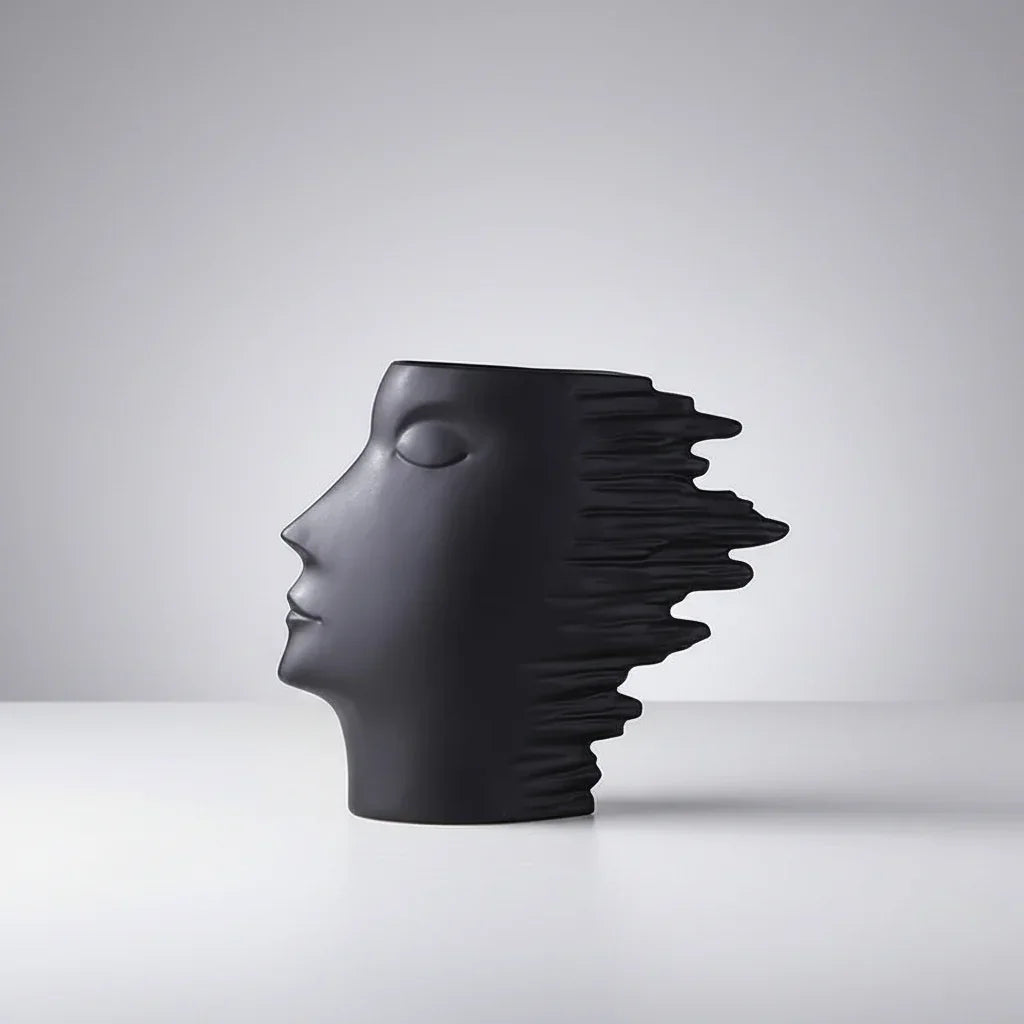 Black ceramic face vase with closed eyes and projecting layered edges, viewed in profile.