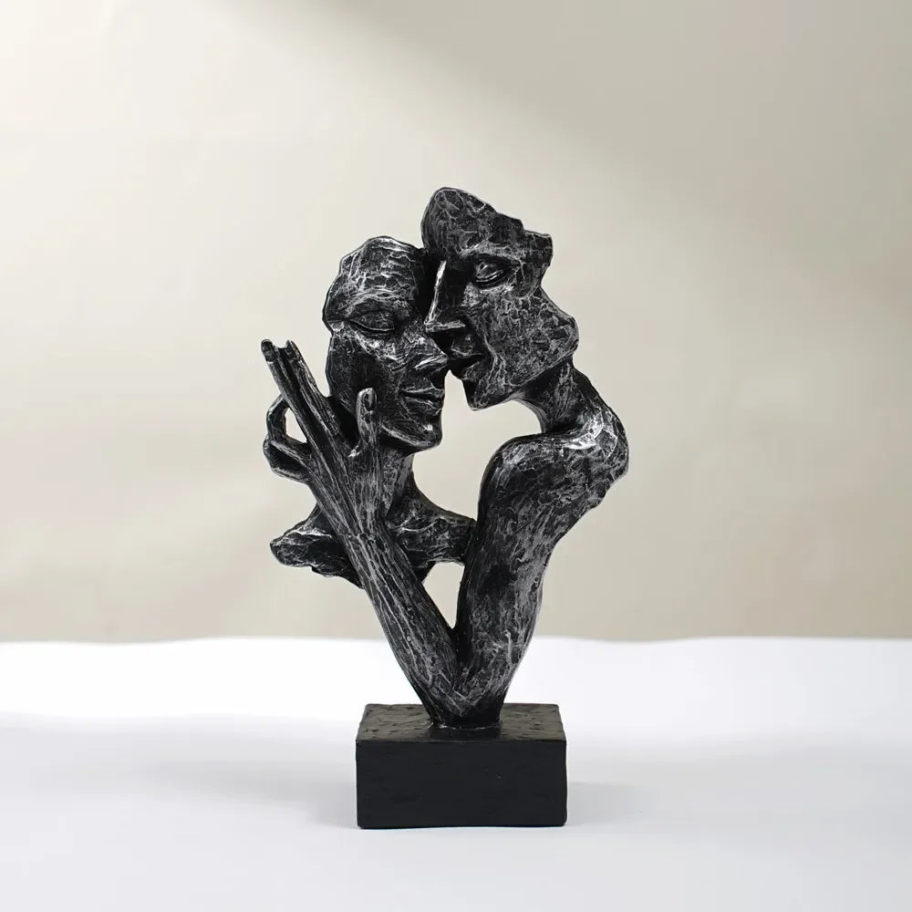Black textured sculpture of two fragmented faces leaning together, with a raised hand and black square base