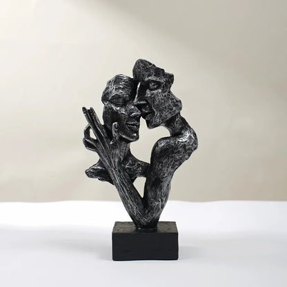 Black textured sculpture of two fragmented faces leaning together, with a raised hand and black square base