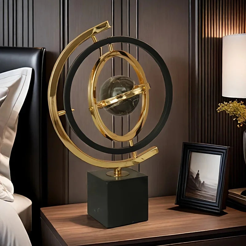 Abstract globe sculpture with black and gold-coloured rings on a cube base beside a framed photograph.