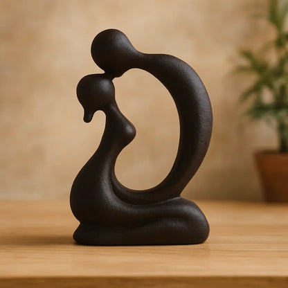 Black abstract kissing couple sculpture with curved seated bodies displayed on a wooden table