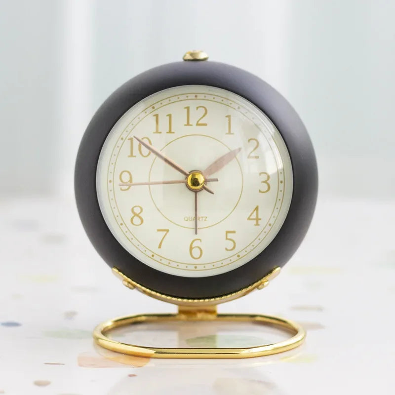 Black round alarm clock with a cream numbered face, gold-coloured hands and circular stand