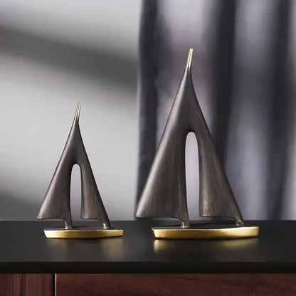 Large and small black sailboat sculptures with gold-coloured bases displayed together on a dark table