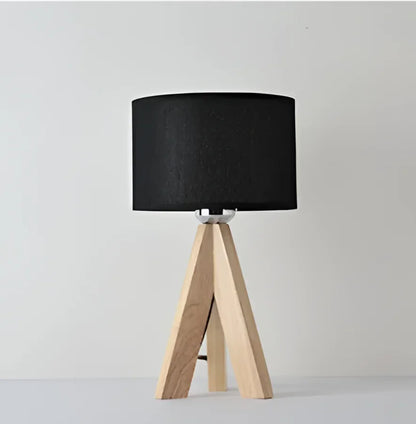 Wooden tripod table lamp with a black cylindrical shade on a plain grey background.