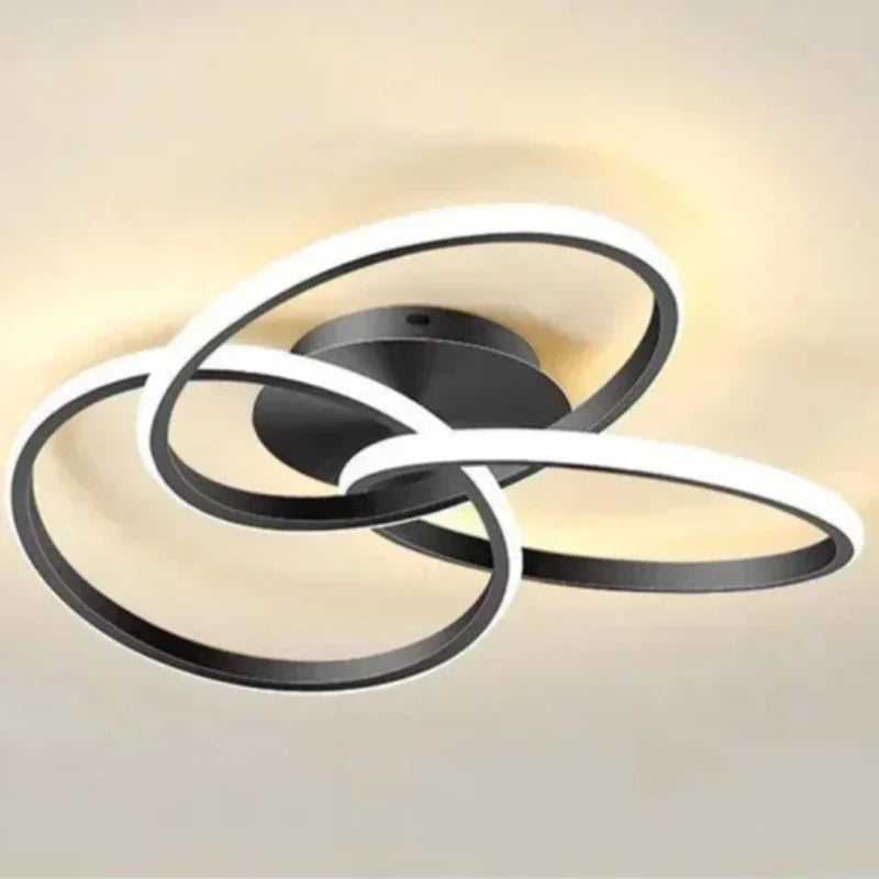 Close-up of a black ceiling light with three intertwined loops and illuminated white LED edges