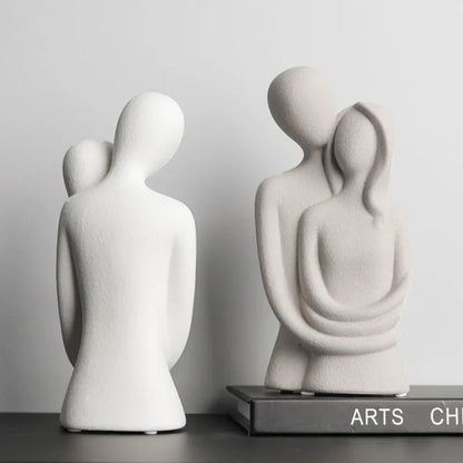 White embracing couple sculpture shown from the back beside a beige sculpture shown from the front