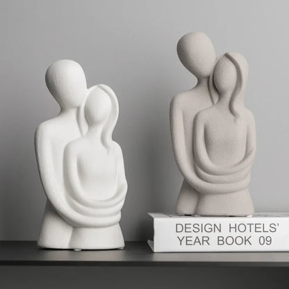 White and beige ceramic sculptures of an embracing couple, one displayed on a book