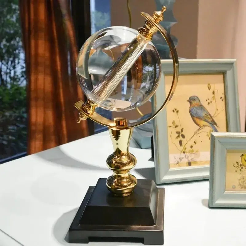 Clear decorative globe with a gold-coloured frame and black base beside framed bird artwork