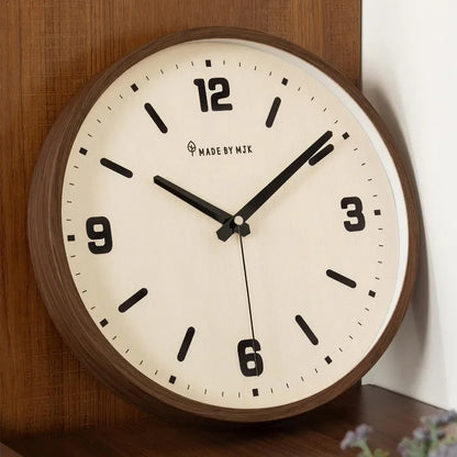 Cream-dial wall clock with a brown rim resting on a table against a wooden panel.