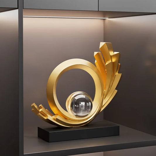 Gold-coloured abstract sculpture with a circular ring, stepped edges and clear sphere on a black base.