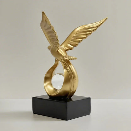 Angled view of the gold-coloured bird sculpture showing raised wings and a clear sphere.