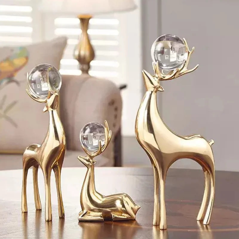 Three gold-coloured deer sculptures, two standing and one reclining, holding clear spheres in their antlers