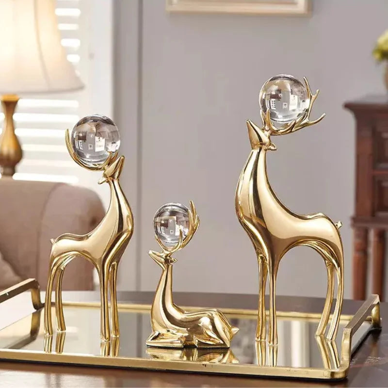 Three gold-coloured deer sculptures with clear spheres held in their antlers on a mirrored tray