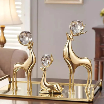 Three gold-coloured deer sculptures with clear spheres held in their antlers on a mirrored tray