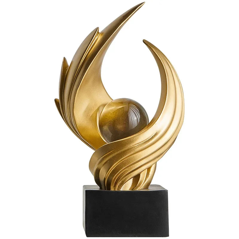 Gold-coloured abstract sculpture with sweeping curves and a clear sphere on a black base against white.