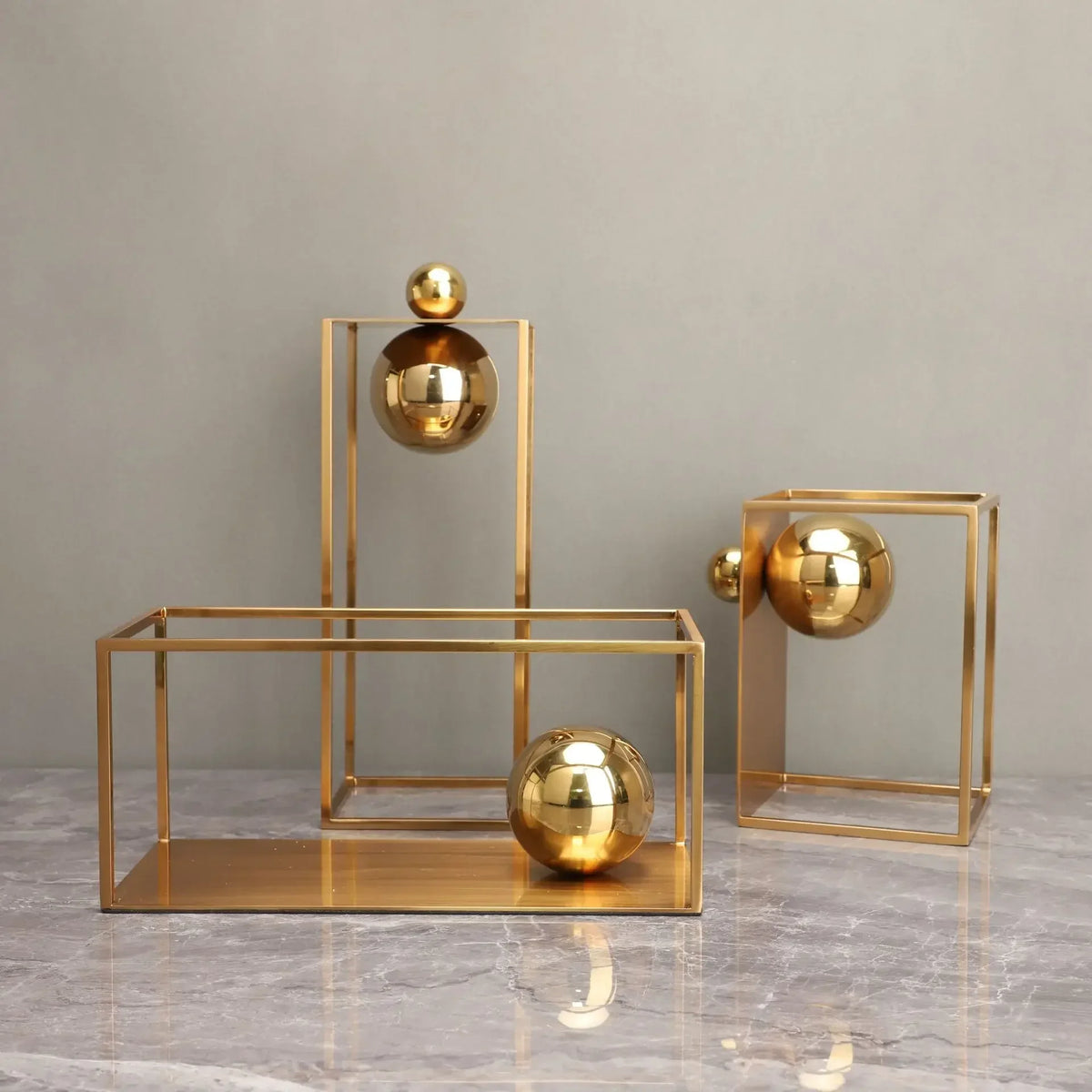 Gold-coloured open geometric frame sculptures with reflective spheres, including one placed horizontally
