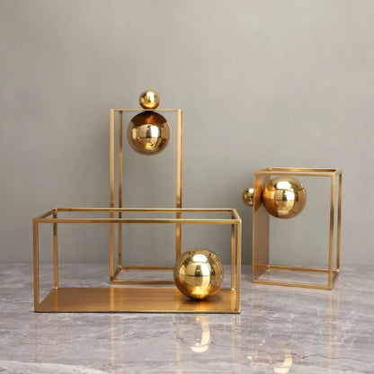 Gold-coloured open geometric frame sculptures with reflective spheres, including one placed horizontally