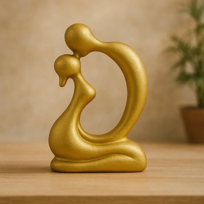 Gold-coloured abstract kissing couple sculpture with curved seated bodies displayed on a wooden table