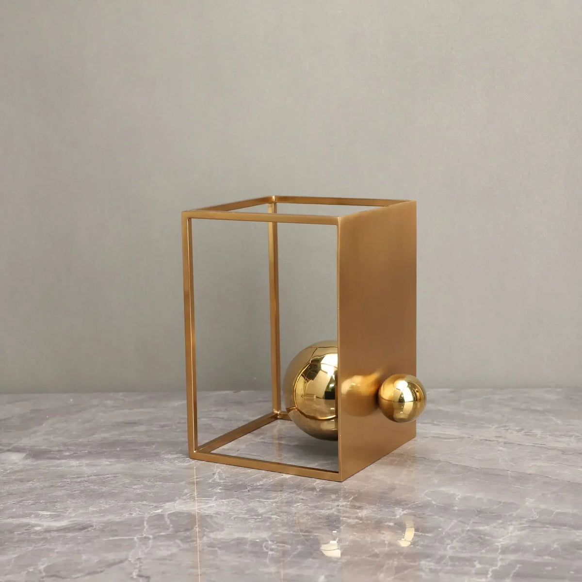 Short gold-coloured open-frame sculpture with a solid side panel and two reflective spheres near its base