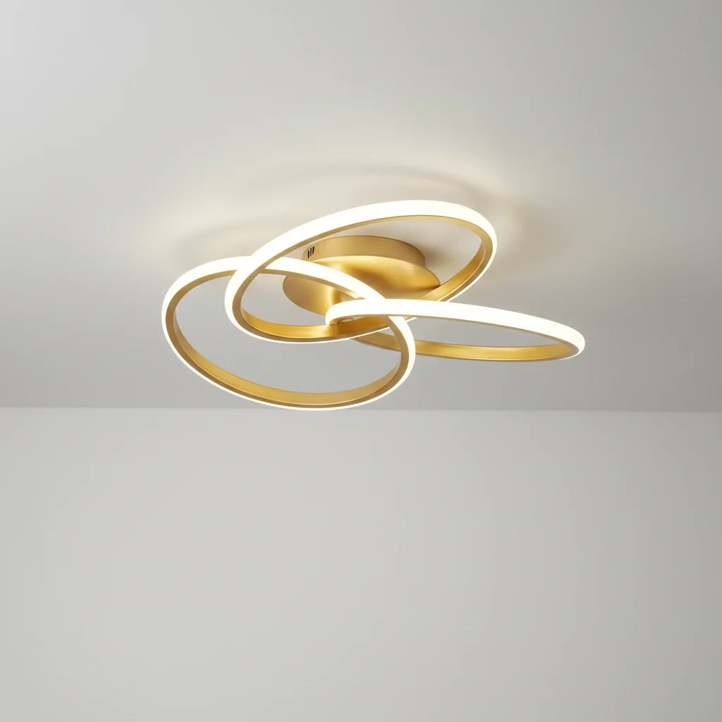 Gold-coloured ceiling light with three intertwined illuminated loops against a white ceiling
