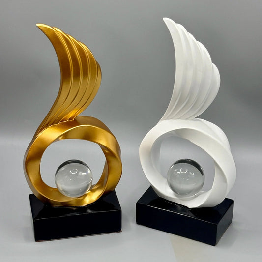 Gold-coloured and white abstract sculptures with tall curved wings and clear spheres on black bases.