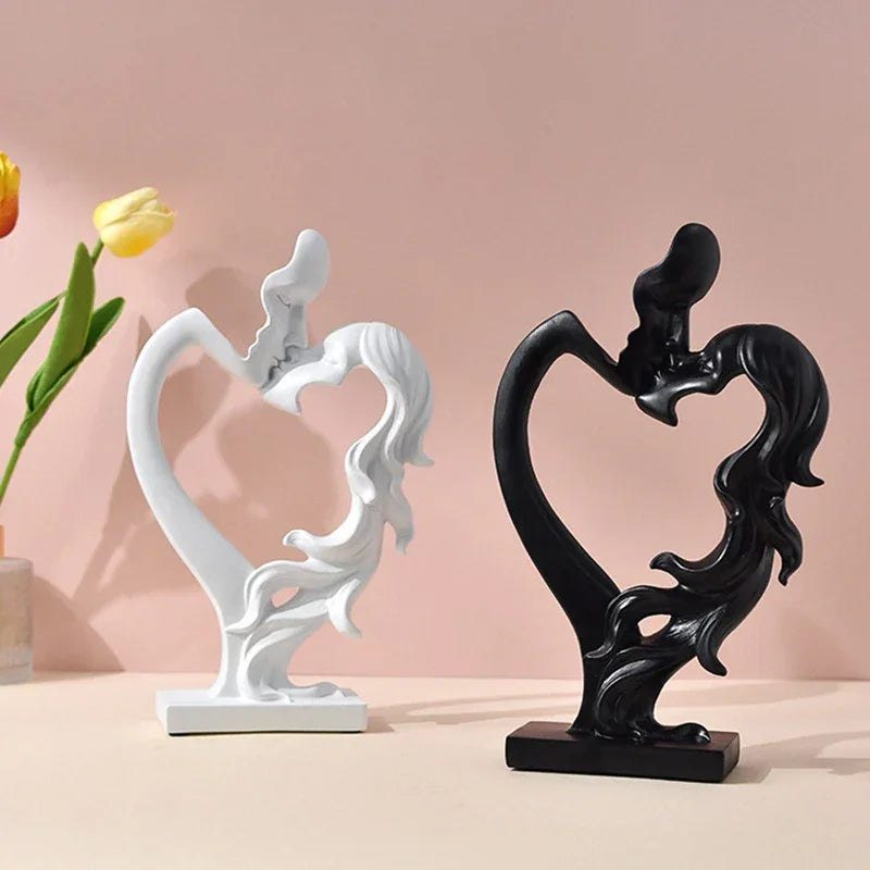 White and black kissing couple sculptures with open heart-shaped centres on a table beside tulips