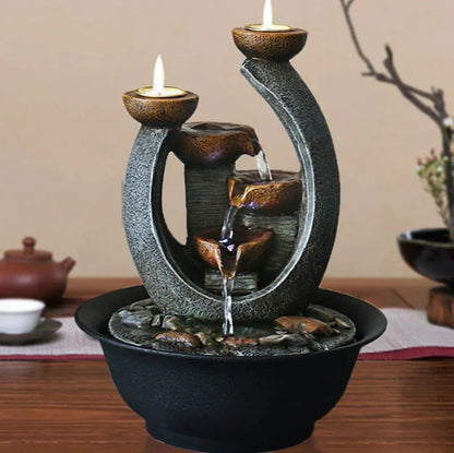 Curved indoor water fountain displayed on a table with two lit candles above its cascading bowls