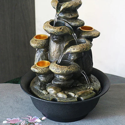 Front view of a stacked rock-style water fountain with gold-coloured candle holders and a black basin