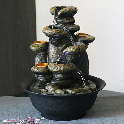 Indoor fountain with water cascading over stacked rock-shaped bowls into a round black basin