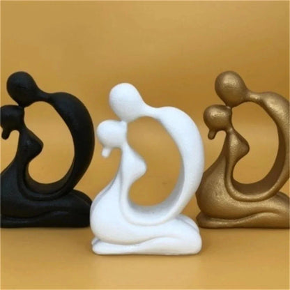 White abstract kissing couple sculpture displayed between black and gold-coloured versions
