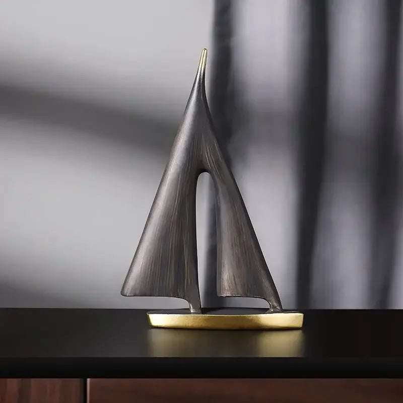 Large black sailboat sculpture with textured triangular sails and a gold-coloured base on a dark table
