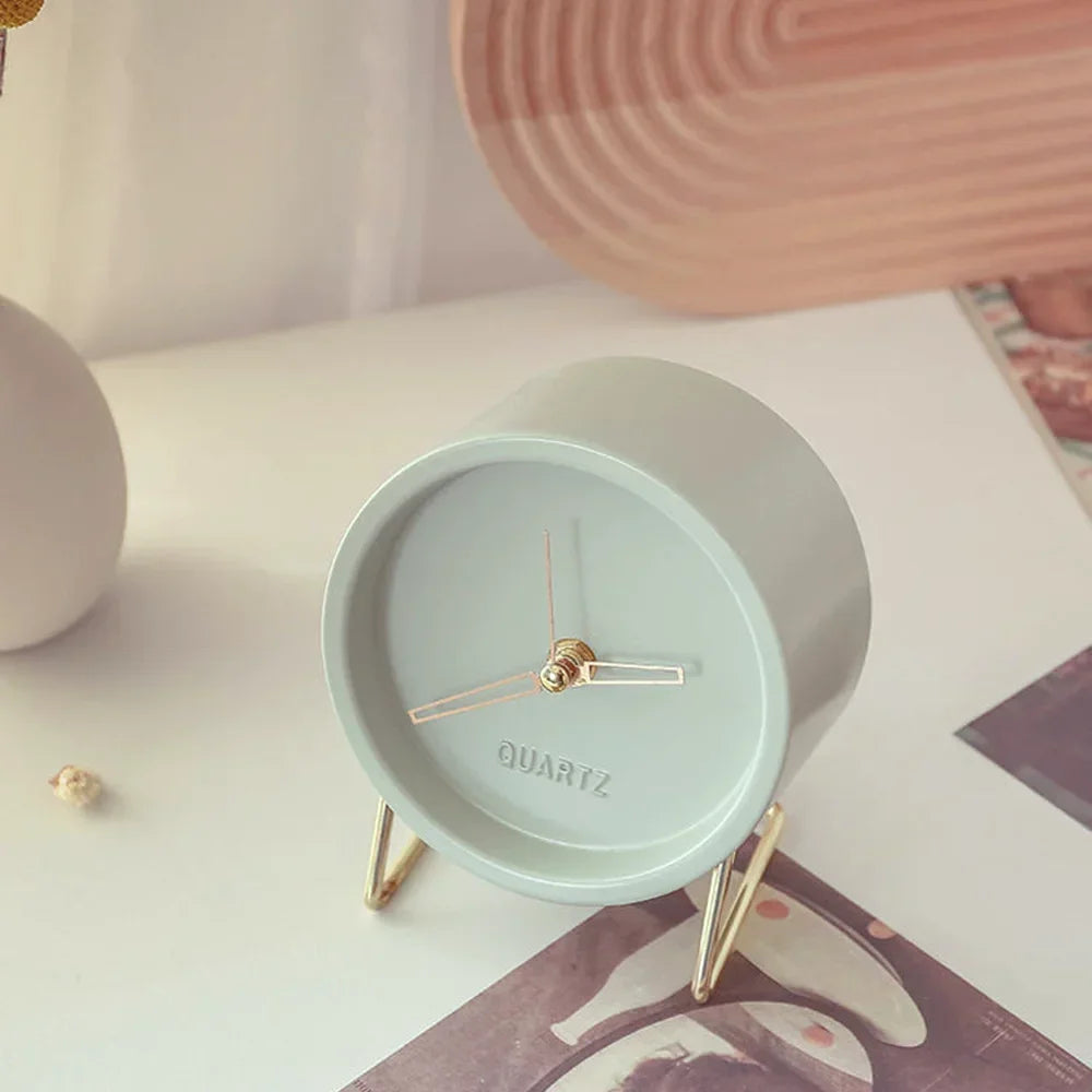 Pale blue round desk clock with gold-coloured hands and a wire stand displayed on a magazine