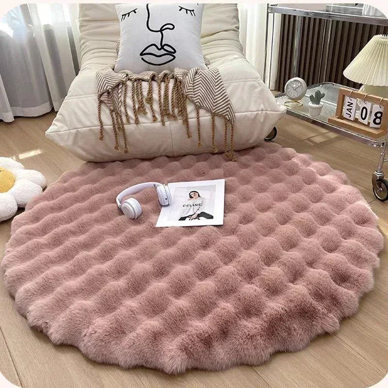 Round pink plush rug with a raised grid pattern in front of an armchair, with headphones and a magazine