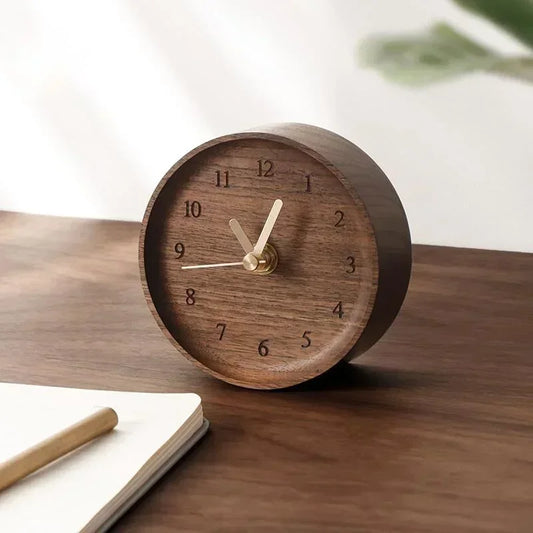 Round walnut desk clock with pale hands and engraved numerals beside a notebook and pencil.