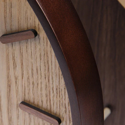 Close-up of a wooden wall clock's dark curved rim, wood-grain face and raised hour markers