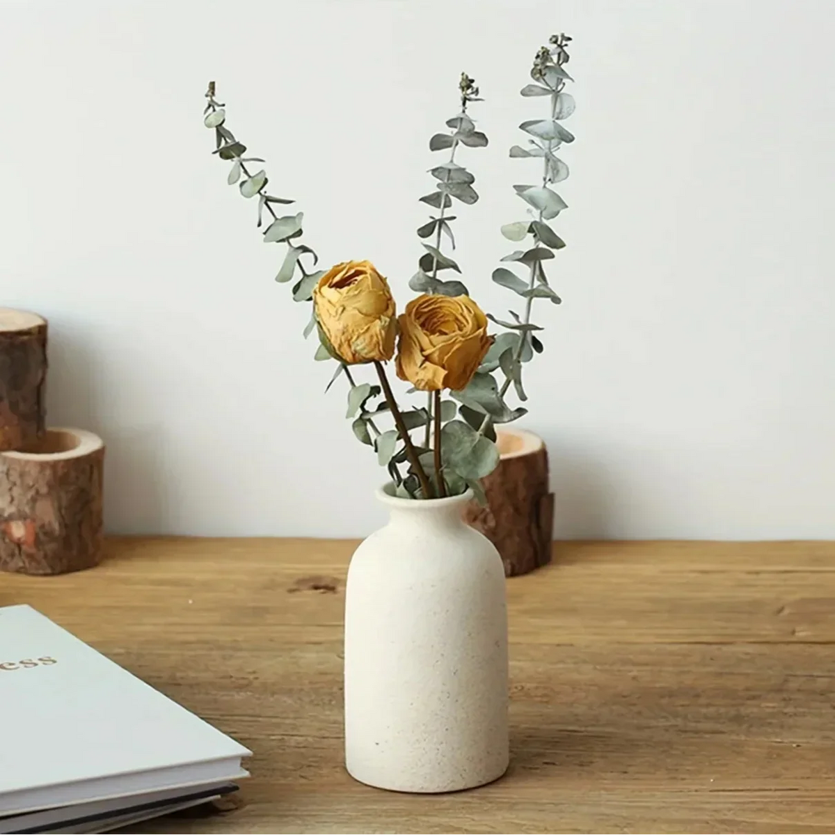 Cream ceramic vase holding dried yellow flowers and green stems on a wooden tabletop