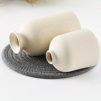 Two cream ceramic vases lying on a round grey mat, showing their narrow openings and speckled surfaces