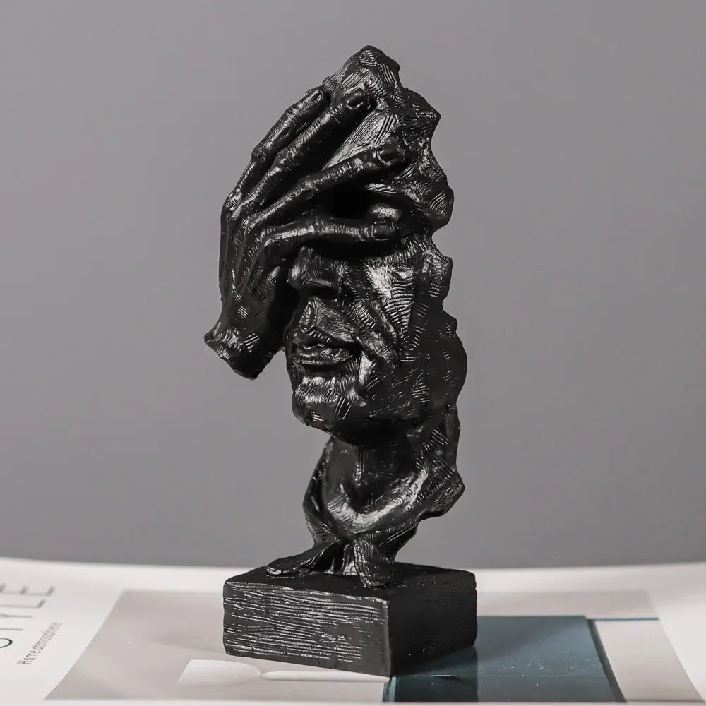 Black textured face sculpture with a hand across its eyes, mounted on a rectangular base