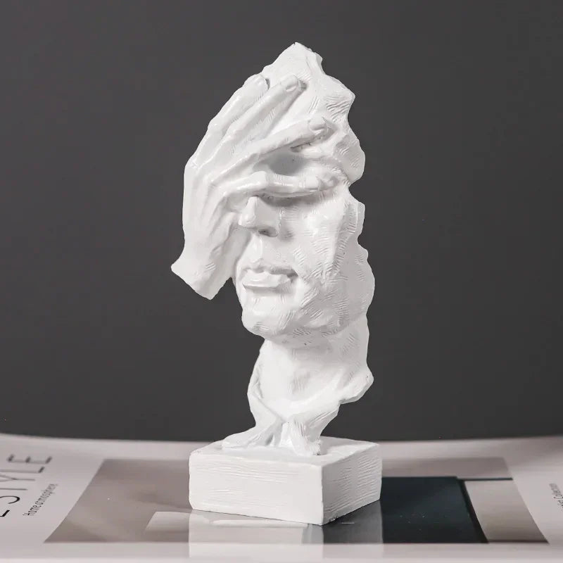 White textured face sculpture with a hand covering its eyes, mounted on a matching white rectangular base