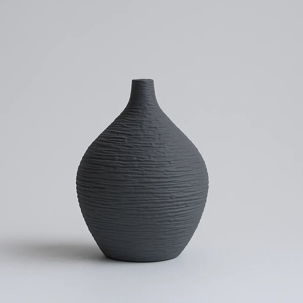 Small charcoal ceramic vase with a rounded textured body and short narrow neck against a grey background