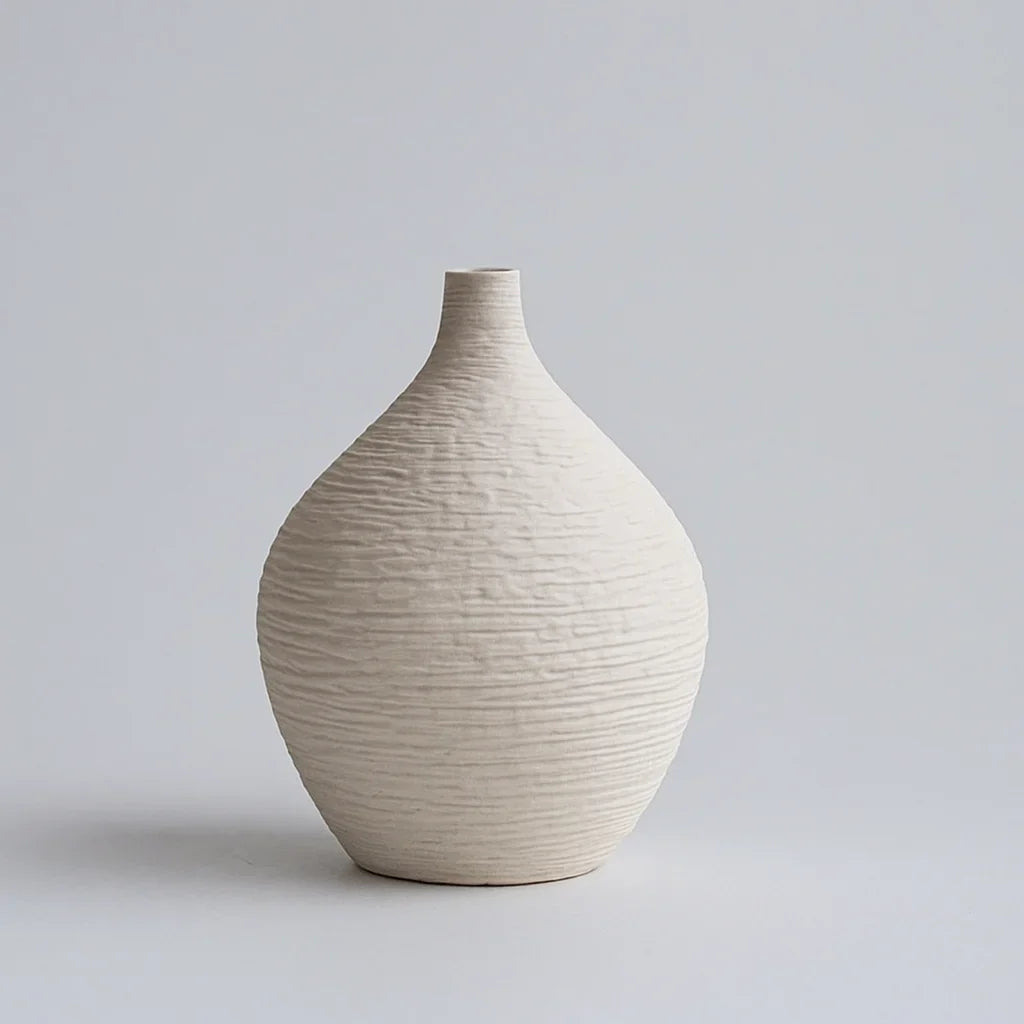 Small white ceramic vase with a rounded textured body and short narrow neck against a grey background