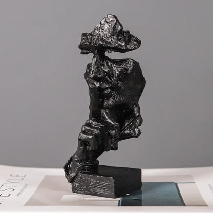 Black fragmented face sculpture with a finger held to its lips, mounted on a rectangular base